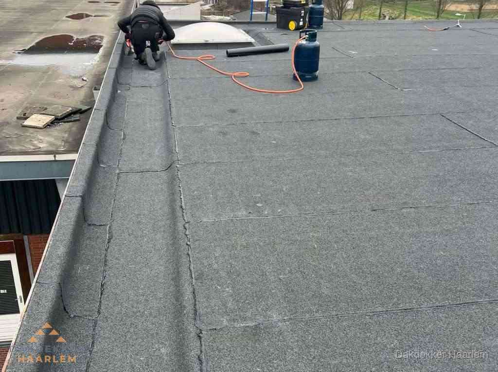 Dakdekker repareert bitumen dakbedekking op groot plat dak in Haarlem